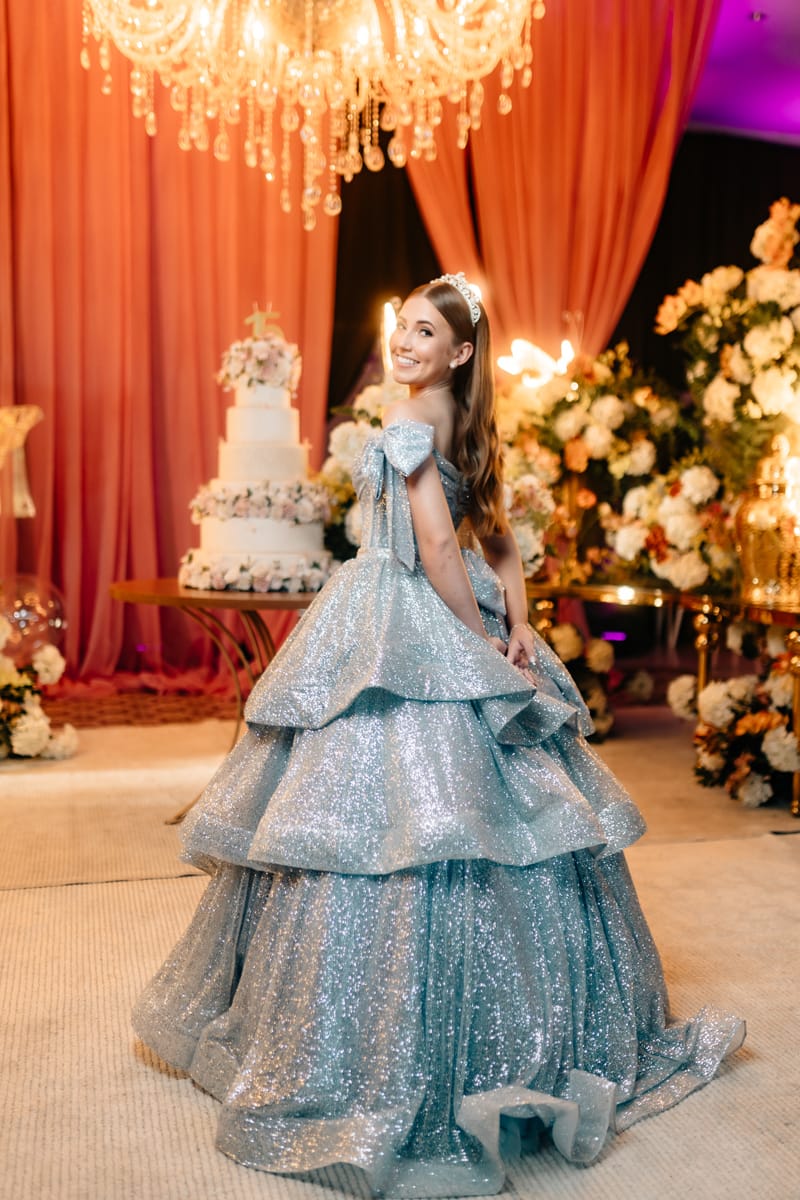 Isadora com vestido de 15 anos, sorrindo com flores e luzes de fundo