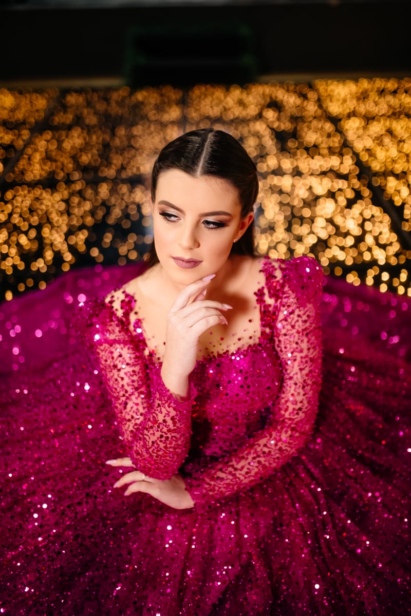 Mariana com vestido de 15 anos, sentada na pista de dança com luzes de fundo